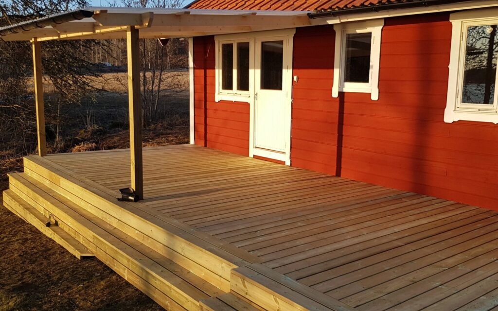 Trädäck och veranda vid rött trähus i Småland
