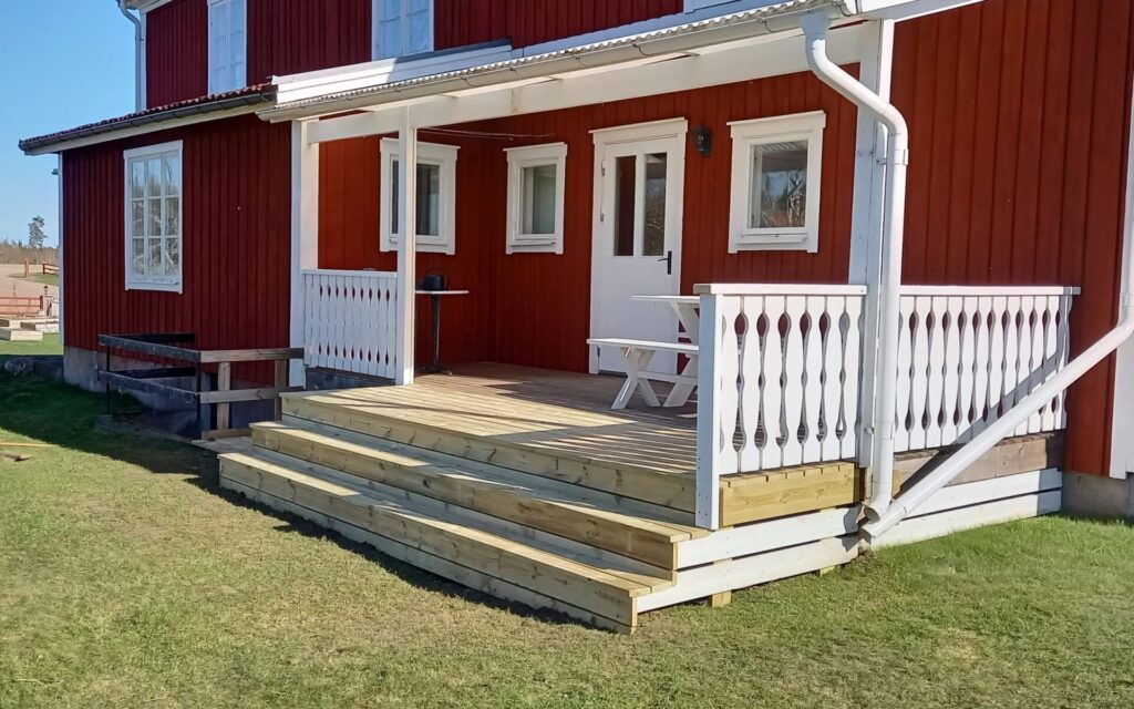 veranda i trä med tak vid ett rött hus i småland